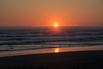 Fototapeta na wymiar Perfect orange setting sun over a perfect beach of crashing waves