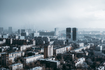 Megapolis cityscape from a high point during heavy rain: residential district in the foreground, low dark thunderclouds, rain in a hazy distance, office business skyscrapers in the middle