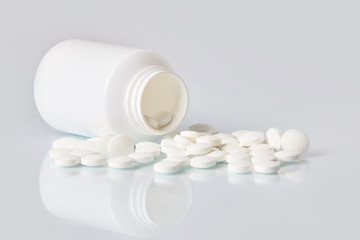 White tablets and pills on white mirror background.  Health care concept.   Scattered supplements...