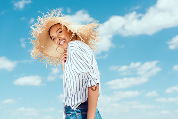 low angle view of smiling african american woman in straw hat against blue cloudy sky