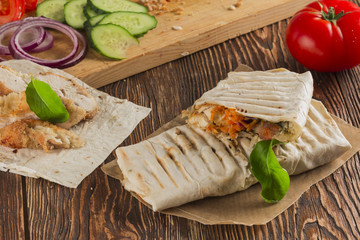 Shaurma, cut in half, meat with vegetables in a bread cake, top view on an old wooden rustic background, on a wooden board with tomato and pepper, copy space