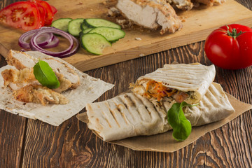 Shaurma, cut in half, meat with vegetables in a bread cake, top view on an old wooden rustic background, on a wooden board with tomato and pepper, copy space