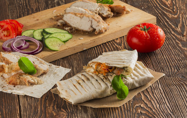 Shaurma, cut in half, meat with vegetables in a bread cake, top view on an old wooden rustic background, on a wooden board with tomato and pepper, copy space