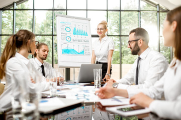 A group of business people strictly dressed in white sitting together during a conference in the spacious office with flip chart on the green background