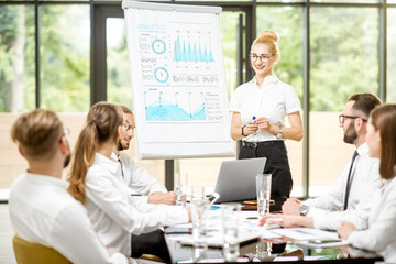 Young woman speaker reporting with flip chart during a conference with business people in the beautiful office on the green background
