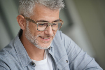 Fototapeta premium Middle-aged guy with trendy eyeglasses reading magazine