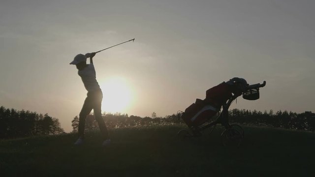 Silhouette of boy golfer with golf bag at sunset