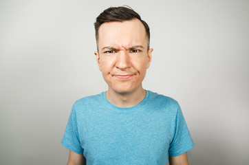 Young unhappy guy with gloomy brows on a light background.