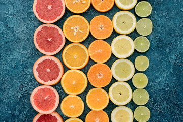 top view of various citrus fruits slices in rows on blue concrete surface
