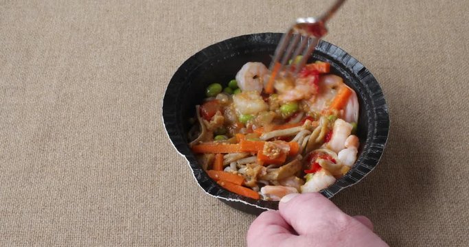 Using a fork to stir a microwaved shrimp vegetables and noodles in a ginger sauce.
