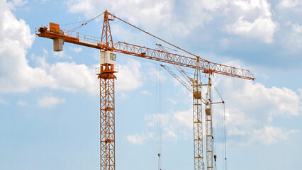 Three construction cranes against blue cloudy sky.