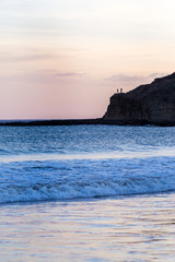 Silhouette of two persons standing on a rock at the beach in the distance. Tranquility concept....
