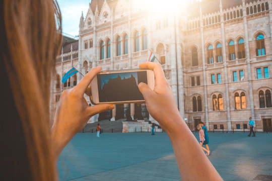 woman taking a picture with her smartphone of parliament building at budapest - holiday scene