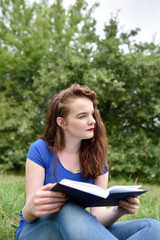 Obraz premium Vertical shot of student reading and dreaming or thinking in a park