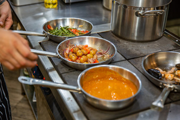 Chef preparing vegetables on frying pan in the professional kitchen.