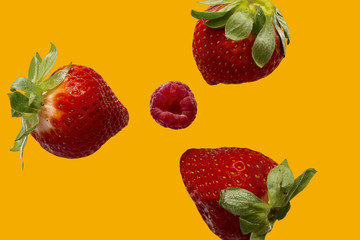 high view of three strawberries with a raspberry in the center with orange background