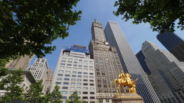 An extreme wide low angle panning establishing shot of the William Tecumseh Sherman Monument near Central Park with the Manhattan skyline in the background. Shot at 60fps.  	