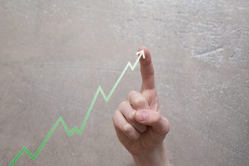 Business development and growing up revenue concept. Finger touching green arrow graph growth or increase business chart on grunge light brown background with copy space for text or image. 