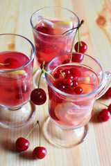 Fresh fruit juice cocktails in three glass cups with red cherries on natural wooden table background. Summer drink.