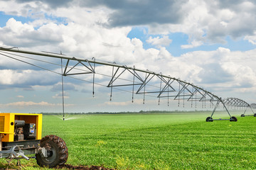 irrigation machine watering agricultural field with young sprouts, green plants on black soil and beautiful sky