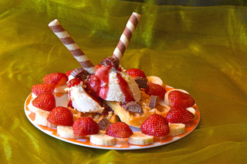 Dessert with ice cream decorated with strawberries, bananas, raspberry sauce and waffles.