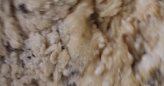 Very close video of stirring ingredients of chocolate chip muffins with a white spoon.