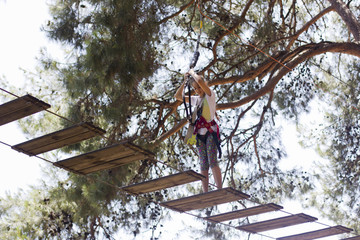 Girl teenager with frightened face with climbing equipment in a rope amusement park