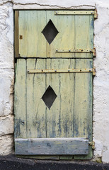 very old green door with peeling paint and rhombic openings in the wood and rusty hinges