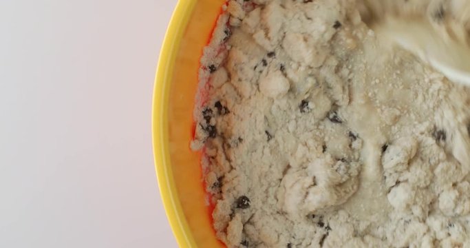 Video of stirring ingredients of chocolate chip muffins with a white spoon in a large yellow mixing bowl atop a counter top.