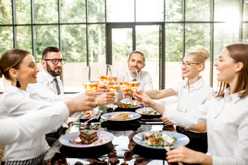 Fototapeta na wymiar Group of business people dressed in white shirts clinking with wine glasses during a business lunch with delicious meals at the modern restaurant