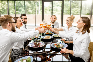 Group of business people dressed in white shirts clinking with wine glasses during a business lunch with delicious meals at the modern restaurant