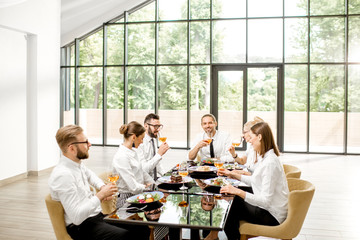Group of business people sitting together during a business lunch at the modern restaurant with big window on the background overlooking on the green park