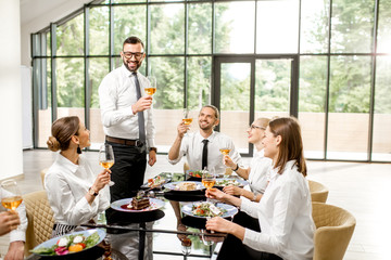 Fototapeta na wymiar Group of business people dressed in white shirts clinking with wine glasses during a business lunch with delicious meals at the modern restaurant