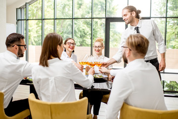Business people dressed in white shirts sitting together during a business lunch with man speaking toast at the modern restaurant