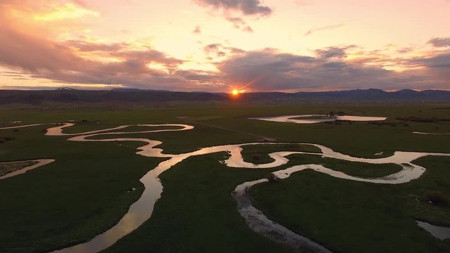 Aerial view flying over winding river during colorful sunset in Star Valley Wyoming.