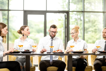 Business people dressed in white shirts having business lunch sitting in a row at the table in the modern restaurant