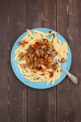 Tasty vegetarian meal. Pasta penne with wild chanterelle mushrooms and chili pepper in blue plate on dark wooden background copyspace