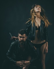 Hipster with beard and sexy girl holds straight razor. Barber with straight razor works on haircut. Barber concept. Couple of sexy girl and brutal bearded hipster with mustache, black background