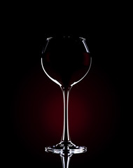 A glass of red wine on a black background with a red gradient in contrasting light