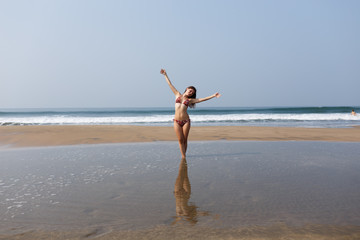 In the background, waves splash in the ocean. The sea horizon. The girl in the swimsuit is pleased with the rest, spreading her hands to the side. The concept of freedom. Pure consciousness. Joy.