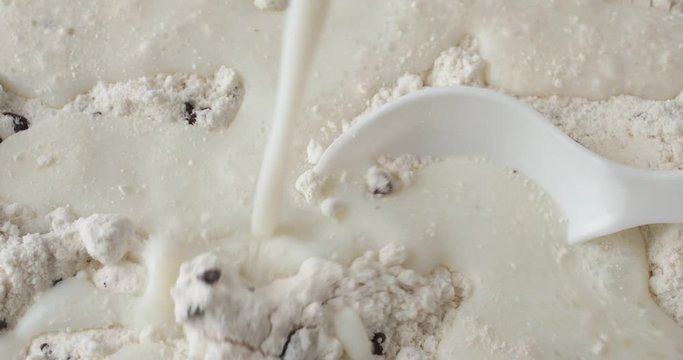 Close video of adding milk to dry clumpy chocolate chip muffin mix in an old ceramic bowl with a white spoon in the food.