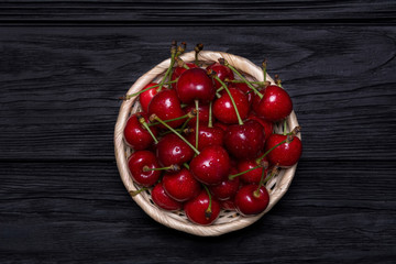 Ripe cherries in a wicker plate on a black wooden background. View from above.