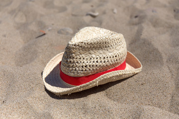 Fototapeta na wymiar Wicker hat with red band laying on the sea sand