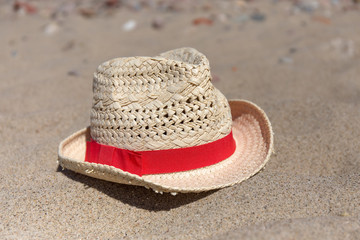 Fototapeta na wymiar Wicker hat with red band laying on the sea sand