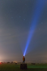A man staying on the haystack in the green field at night.  Light ray pointing to stars