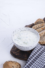Yoghurt with cucumber. Fresh dip of famous Greek taziki with cucumber. fresh bread, towel and white background. Copy space.
