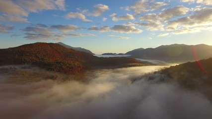 Sunrise mountain aerial with golden light through dense low fog