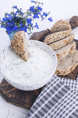 Yoghurt with cucumber. Fresh dip of famous Greek taziki with cucumber. fresh bread, towel and white background. Copy space