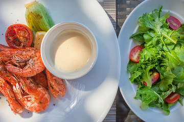 Grilled shrimps on plate with sauce and plate with green salad with tomato. Top view