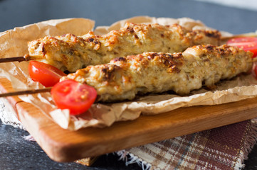 Kebab on a paper napkin with cherry tomatoes on a wooden background. Prepared traditional meat. Soft focus.